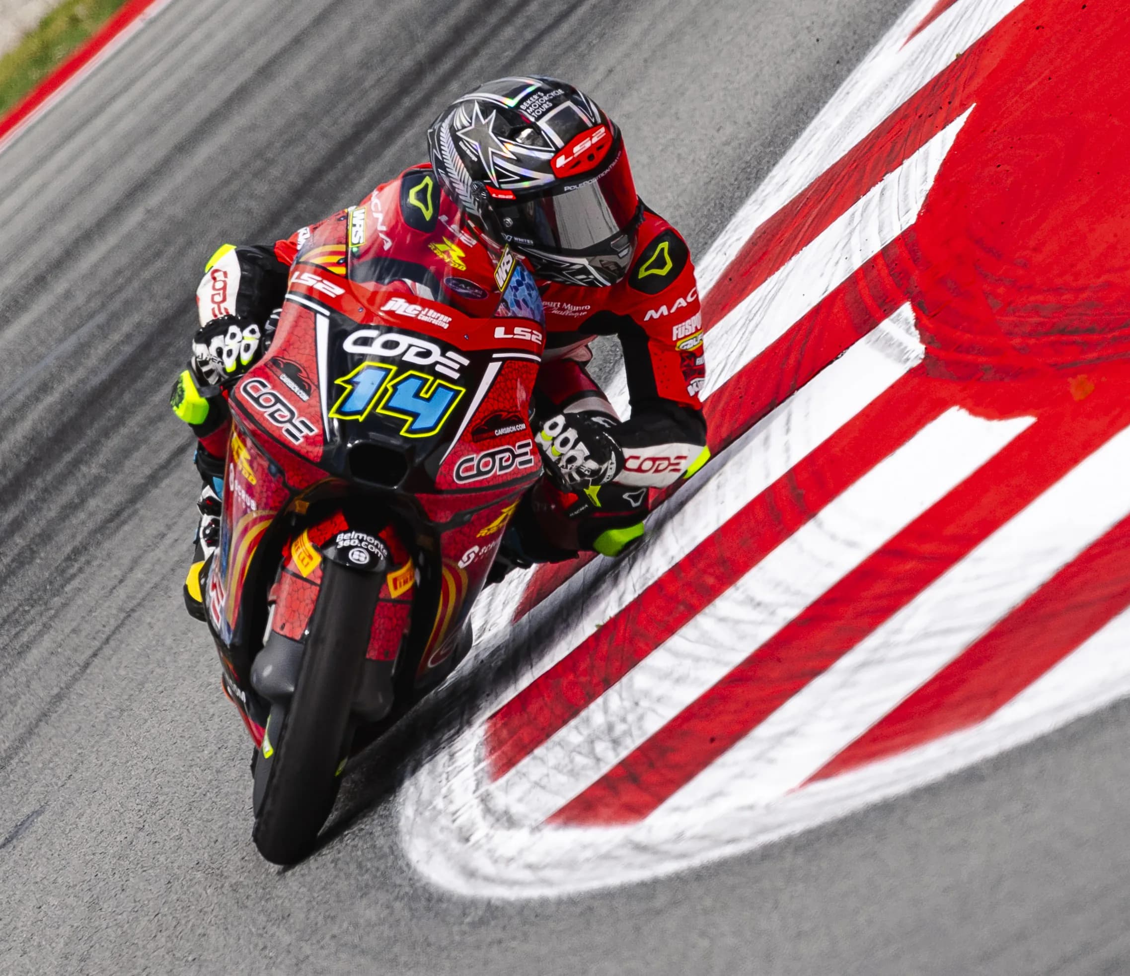 Cormac Buchanan leaning his red number 14 CODE Moto3 bike over a red and white kerb at Barcelona