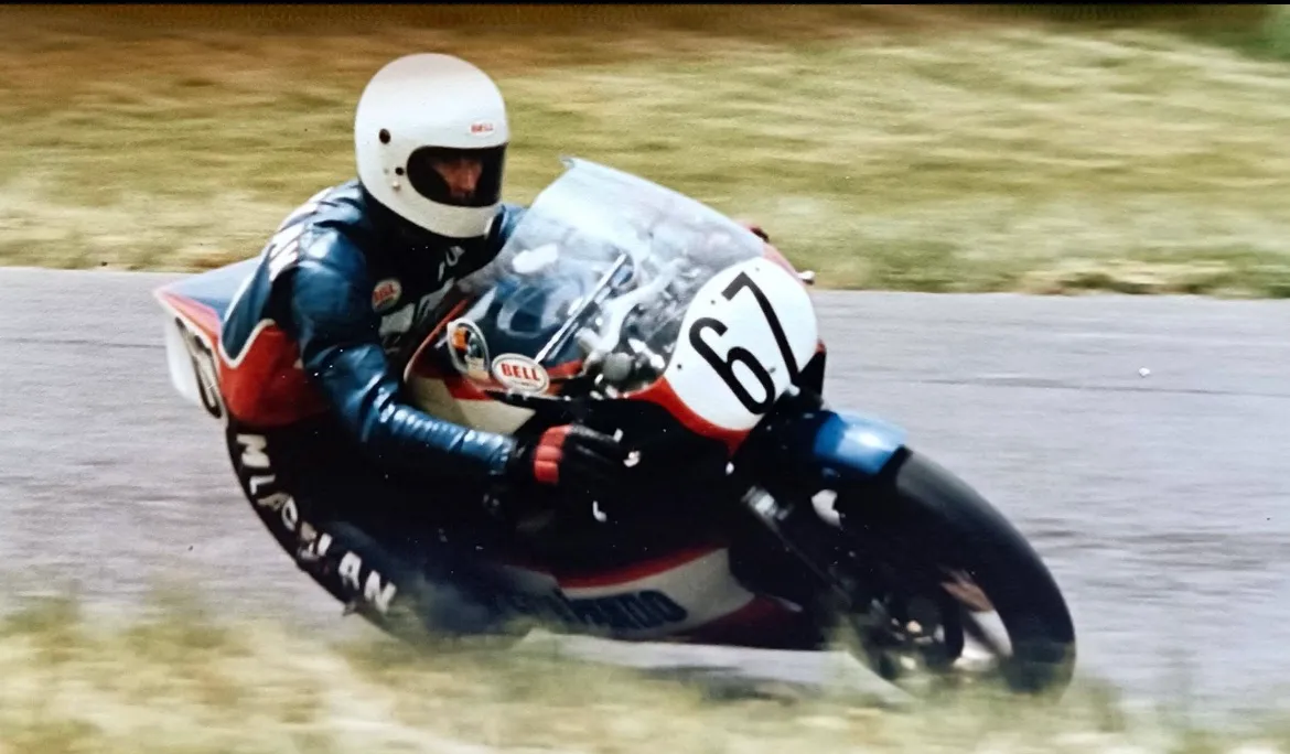 Paul McLachlan leaning a race bike, number 67, through a corner in a vintage photo